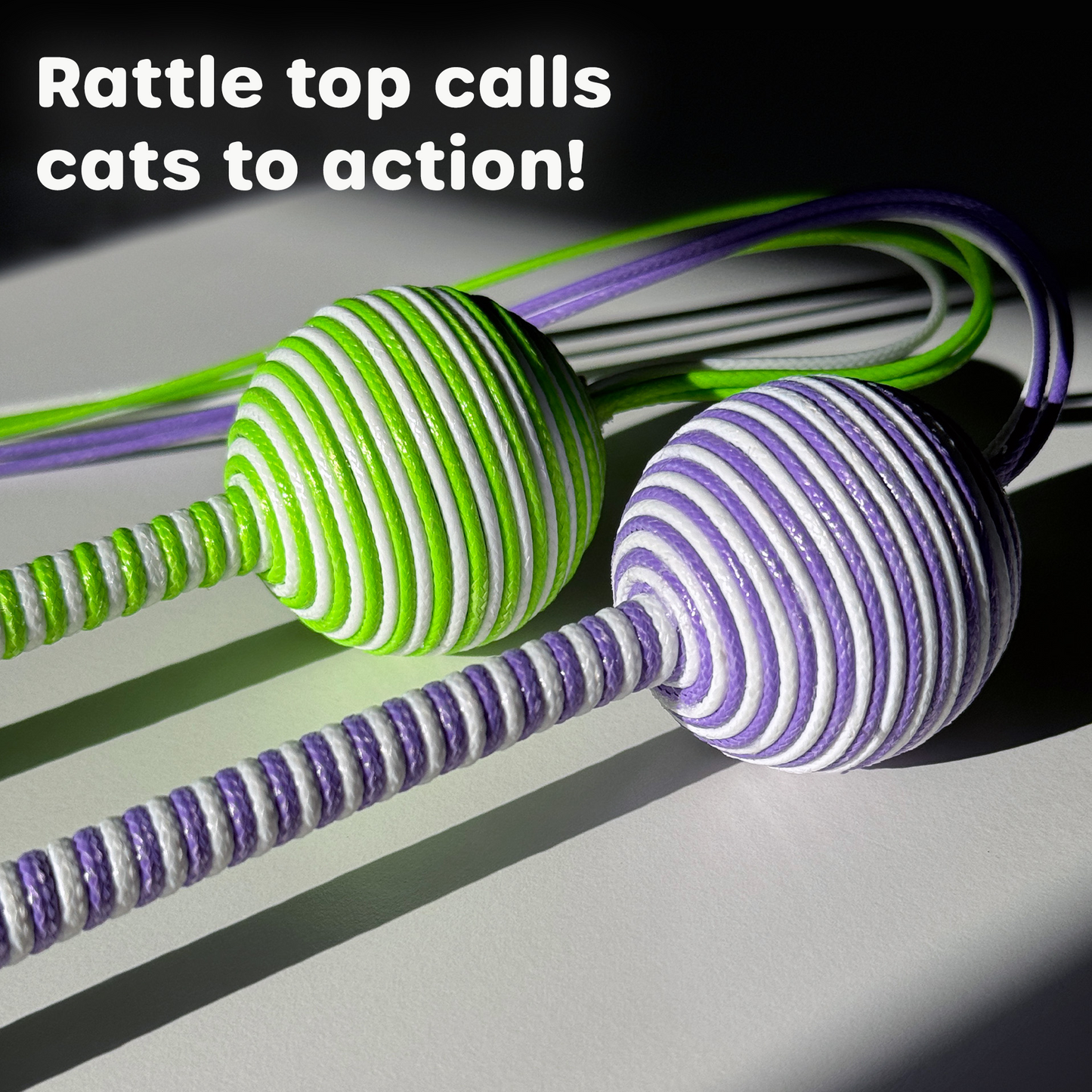 Close-up image showing the green and purple rattle tops of the Wiggle Wand™ Cat Toys side by side, with text 'Rattle top calls cats to action!' displayed at the top, highlighting the toy's engaging sound feature.